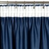 Granatowa zasłona z białym, przezroczystym pasem u góry, zawieszona na metalowym karniszu za pomocą metalowych klipsów. Materiał zasłony ma delikatną fakturę, a górna część jest marszczona.