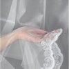 Przezroczysta firana w kolorze białym z delikatnym, falistym wzorem na brzegu jest trzymana w dłoni. Tkanina ma subtelną fakturę, która przepuszcza światło, tworząc elegancki efekt.