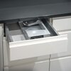 Na zdjęciu znajduje się krajalnica w kolorze srebrnym z czarnym pokrętłem regulacji grubości krojenia, oznaczonym cyframi od 0 do 6. Na składanej części urządzenia widoczny jest napis "tiny".