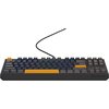 Przedstawiona jest klawiatura mechaniczna z podświetleniem RGB, posiadająca ciemne klawisze z kilkoma wyróżniającymi się pomarańczowymi klawiszami. Na obudowie klawiatury widoczne jest logo "GENESIS".