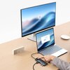 Na zdjęciu znajduje się biurko z laptopem, zewnętrznym monitorem i hubem USB, do którego podłączone są różne kable. Na ekranie monitora widoczny jest ekran logowania z ikoną użytkownika i napisem "Business", a na biurku stoi cyfrowy zegar.