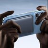 Na zdjęciu widoczny jest telefon trzymany w dłoniach, do którego z tyłu przymocowany jest stalowy powerbank. Powerbank ma gładką powierzchnię i jest umieszczony centralnie na obudowie telefonu.