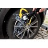 Na zdjęciu widać koło samochodowe, które jest czyszczone szczotką do felg z napisem "DUNLOP" na uchwycie. Woda rozpryskuje się wokół felgi, a żółta strzałka wskazuje kierunek ruchu szczotki.