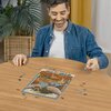 Na zdjęciu widać osobę układającą puzzle na okrągłym, drewnianym stole. Puzzle przedstawiają kolorową scenę z filmu "Dumbo" i są częściowo ułożone, a wokół leżą pojedyncze elementy.