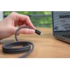 Na zdjęciu widać rękę trzymającą szary kabel USB-C z napisem "XLINE" na wtyczce, obok laptopa na drewnianym stole. Na ekranie laptopa widoczny jest fragment strony z tekstem "Rekomendowane do" oraz "25W".
