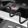 Zbliżenie na czarny, pleciony kabel USB, który jest częściowo zwinięty. W tle widoczne są dwa porty USB z czerwonym wnętrzem oraz przyciski z napisami "MEDIA" i "HOME".