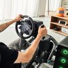 Osoba siedzi w symulatorze wyścigowym, trzymając kierownicę i dźwignię zmiany biegów kontrolera LOGITECH RS Shifter & Handbrake. W tle widoczny jest pomarańczowy kask na półce oraz urządzenia elektroniczne.