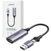 Na zdjęciu znajduje się rejestrator obrazu UGREEN CM489 z kablem USB i HDMI, obok którego widoczne jest opakowanie z napisem "UGREEN" oraz tekstem w języku chińskim i angielskim: "USB 高清视频采集卡 HD USB Video Capture Card". Produkt ma metaliczną obudowę i jes