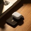 Na zdjęciu znajduje się czarny powerbank z białym etui na słuchawki umieszczonym na jego powierzchni. Obok leży smartfon z trzema obiektywami aparatu, a całość spoczywa na drewnianym blacie.