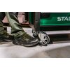 Na zdjęciu widoczne są czarne półbuty robocze z żółtymi sznurówkami, obok zielonego wózka z napisem "STALCO" na boku. Wózek ma metalowe kółka, a osoba nosi zielone spodnie robocze.