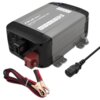 Na zdjęciu znajduje się inteligentna ładowarka QOLTEC 51952 z widocznymi oznaczeniami technicznymi na obudowie, w tym "BATTERY CHARGER 10A". Obok ładowarki leży kabel z zaciskami oraz przewód zasilający.