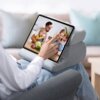 Na zdjęciu widoczna jest podstawka do tabletu UGREEN LP473, na której umieszczony jest tablet wyświetlający obraz rodziny przy stole. Podstawka ma szary kolor i znajduje się na kolanach osoby siedzącej na sofie.