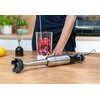 Na drewnianym blacie kuchennym leży srebrno-czarny blender ręczny, obok którego stoi wysoki pojemnik z malinami i mlekiem. W tle widoczna jest trzepaczka oraz cytryna, a także rozmyte elementy kuchni.