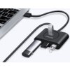 Na zdjęciu widoczny jest czarny hub USB z kilkoma podłączonymi urządzeniami, w tym pendrive'ami, połączony kablem z laptopem. Na hubie znajduje się logo "UGREEN".