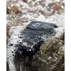 Na zdjęciu widać smartfon leżący na kamieniach, częściowo zanurzony w wodzie, z widocznymi kroplami na jego powierzchni. W tle rozmyte kamienie i woda tworzą efekt bokeh.