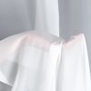 Na zdjęciu widoczna jest biała firana o delikatnej, półprzezroczystej strukturze, która układa się miękko na tle szarej powierzchni. Materiał firany jest lekki i zwiewny, co nadaje jej elegancki wygląd.