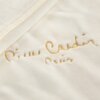 Kremowy materiał z haftowanym złotym napisem "Pierre Cardin Paris". Widoczna jest tekstura tkaniny oraz delikatne marszczenia.