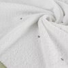 Biały ręcznik o fakturze frotte z delikatnymi, zielonymi kropkami rozmieszczonymi na powierzchni. Materiał jest miękki i puszysty, z widocznymi zagięciami i fałdami.