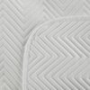 Zdjęcie przedstawia białą narzutę z wyraźnym, geometrycznym wzorem w jodełkę. Materiał ma teksturę przypominającą len, co nadaje mu elegancki wygląd.