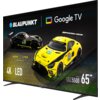 Na zdjęciu widoczny jest telewizor z logo "BLAUPUNKT" oraz "Google TV", na ekranie którego wyświetlane są dwa samochody wyścigowe z napisami "IRON LYNX" i "4K | LED". W dolnym rogu znajduje się oznaczenie "UGC5500 Series 65"".