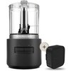 Czarny malakser KitchenAid z przezroczystym pojemnikiem i dwoma przyciskami oznaczonymi cyframi 1 i 2, obok znajduje się czarny akumulator. Na urządzeniu i akumulatorze widoczne jest logo "KitchenAid".
