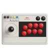 Kontroler arcade stick w jasnym kolorze z czerwonymi przyciskami i czarną gałką joysticka. Na panelu widoczny jest napis "8BitDo Arcade Stick" oraz różnokolorowe przyciski funkcyjne i przełączniki.