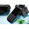 Telefon komórkowy z klawiaturą numeryczną i ekranem, na którym widnieje logo "ulefone", leży na niebieskim tle obok czarnych skał i zielonej rośliny.