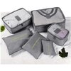 Na zdjęciu znajduje się zestaw sześciu szarych organizerów, z których trzy mają napis "LAUNDRY POUCH" w kolorze żółtym. Organizery są ułożone na jasnym tle, a obok nich widoczne są zielone liście.