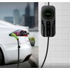 Na zdjęciu widoczny jest biały samochód elektryczny podłączony do ładowarki ściennej z logo "Qoltec" i napisem "EV CHARGER". Ładowarka ma czarną obudowę z zielonymi elementami i wyświetlaczem.