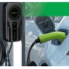 Na zdjęciu widoczna jest ładowarka do samochodu elektrycznego z logo "Qoltec" oraz zielona wtyczka podłączona do pojazdu. W tle pada deszcz, a na ładowarce znajdują się przyciski i wskaźniki.