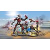 Na zdjęciu znajduje się zestaw klocków LEGO przedstawiający scenę bitwy z serii Marvel, z dużą figurką robota i kilkoma mniejszymi postaciami w dynamicznych pozach. W tle widoczne są elementy scenerii, takie jak wieża kontrolna i płomienie, a na jednym z 