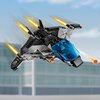Na zdjęciu znajduje się model samolotu z klocków LEGO, z przezroczystą niebieską kabiną, w której widoczna jest figurka. Samolot jest w ruchu, z widocznymi efektami ognia z silników, a w tle znajduje się rozmyty budynek.