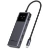 Na zdjęciu znajduje się hub UGREEN Uno CM888 6w1 USB Typu C z ciemnym wyświetlaczem i kilkoma portami USB, a także zintegrowanym kablem zakończonym wtykiem USB-C. Na obudowie widoczny jest napis "UGREEN Uno".
