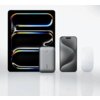 Na zdjęciu znajduje się szary powerbank z napisem "AUKEY" na tle urządzeń elektronicznych, w tym dużego ekranu z kolorowymi wzorami. Obok powerbanka widoczne są dwa inne urządzenia o nowoczesnym designie.