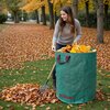 Na zdjęciu widoczny jest zielony worek na liście z czerwonymi uchwytami, wypełniony żółtymi liśćmi. W tle znajduje się trawnik pokryty opadłymi liśćmi oraz drzewa z jesiennymi liśćmi.