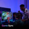 Na zdjęciu widać dwóch graczy przed monitorem, na którym wyświetlana jest gra komputerowa z napisem "PENTAKILL!". W dolnej części zdjęcia znajduje się tekst "Game Sync".