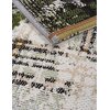 Zbliżenie na teksturę dywanu wewnętrznego z widocznymi detalami splotu w kolorach zielonym, czarnym, białym i brązowym. Krawędzie dywanu są starannie obszyte, a wzór jest geometryczny i złożony.