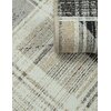 Zdjęcie przedstawia fragment dywanu zewnętrznego o wzorze w odcieniach żółci, szarości i czerni, z widoczną teksturą tkaniny i zrolowanym brzegiem. Wzór dywanu składa się z geometrycznych kształtów i linii, tworzących złożony, nowoczesny design.