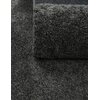 Zdjęcie przedstawia zbliżenie na ciemnoszary, teksturowany dywan o gęstym splocie, częściowo zwinięty. Widoczna jest struktura materiału, która nadaje mu puszysty wygląd.