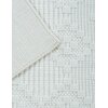 Zdjęcie przedstawia fragment kremowego dywanu o marokańskim wzorze, z widoczną teksturą splotu i wywiniętym rogiem ukazującym spód. Dywan ma wyraźny, geometryczny wzór złożony z wypukłych elementów.