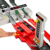Na zdjęciu znajduje się tor wyścigowy z serii Hot Wheels z dwoma małymi samochodzikami na czerwonym odcinku toru. Widoczne są napisy "Formula 1" oraz liczby od 6 do 1 na pionowej tablicy, a także ręka naciskająca żółty przycisk.