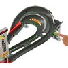 Zdjęcie przedstawia tor wyścigowy z serii Hot Wheels, z zakrętem i oznaczeniami toru, w tym logo "Pirelli" oraz zielonymi strzałkami. Widoczna jest ręka naciskająca zielony przycisk, a obok znajduje się pionowa tablica z numerami od 1 do 5.
