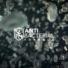 Na zdjęciu widoczne są powiększone grafiki bakterii na niebieskim tle oraz obok nich napis "ANTI BACTERIAL FORMULA" z ikoną tarczy. Tło napisu jest w odcieniach zieleni i niebieskiego, z delikatnym wzorem fal.