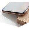 Zbliżenie na krawędź smartfona z założonym szkłem hartowanym, leżącego na drewnianej powierzchni. Telefon ma metaliczną ramkę i widoczny jest fragment ekranu oraz przycisk boczny.