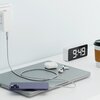 Na zdjęciu znajduje się szary kabel USB Typ-C - Lightning QUALO Ultimate QKN-CL-18 o długości 1,5 m, podłączony do fioletowego telefonu leżącego na zamkniętym laptopie. Obok widoczny jest zegar elektroniczny z wyświetlaną godziną 9:49, etui na słuchawki, 