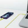 Na zdjęciu widać żółty kabel USB-C - USB-C podłączony do fioletowego smartfona i laptopa. Na ekranie smartfona wyświetla się ikona ładowania oraz napis "100%".