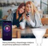 Dwie osoby siedzą przy drewnianym stole, patrząc na telefon, obok którego widoczny jest ekran aplikacji do sterowania żarówką z kolorowym kołem i suwakami jasności oraz temperatury. Na dole zdjęcia znajduje się napis: "Steruj żarówką z dowolnego miejsca za pomocą aplikacji w telefonie" oraz obraz żarówki LED.