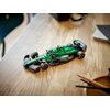 Na zdjęciu znajduje się model bolidu F1 z klocków LEGO w kolorze zielonym z czarnymi i żółtymi detalami, umieszczony na drewnianym stole. Na bolidzie widoczne są napisy: "aramco" oraz "cognizant".