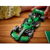 Na zdjęciu znajduje się zielony model bolidu F1 z klocków LEGO, umieszczony na drewnianej powierzchni. Na bolidzie widoczne są napisy: "KICK", "einfach", "sauber", "team", a w tle widać rozmyty fragment jasnego materiału.