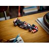 Na zdjęciu znajduje się model bolidu F1 z serii LEGO Speed Champions, umieszczony na drewnianym blacie. Na bolidzie widoczne są napisy "HAAS" oraz logo "MoneyGram", a w tle znajdują się książki i notatnik.